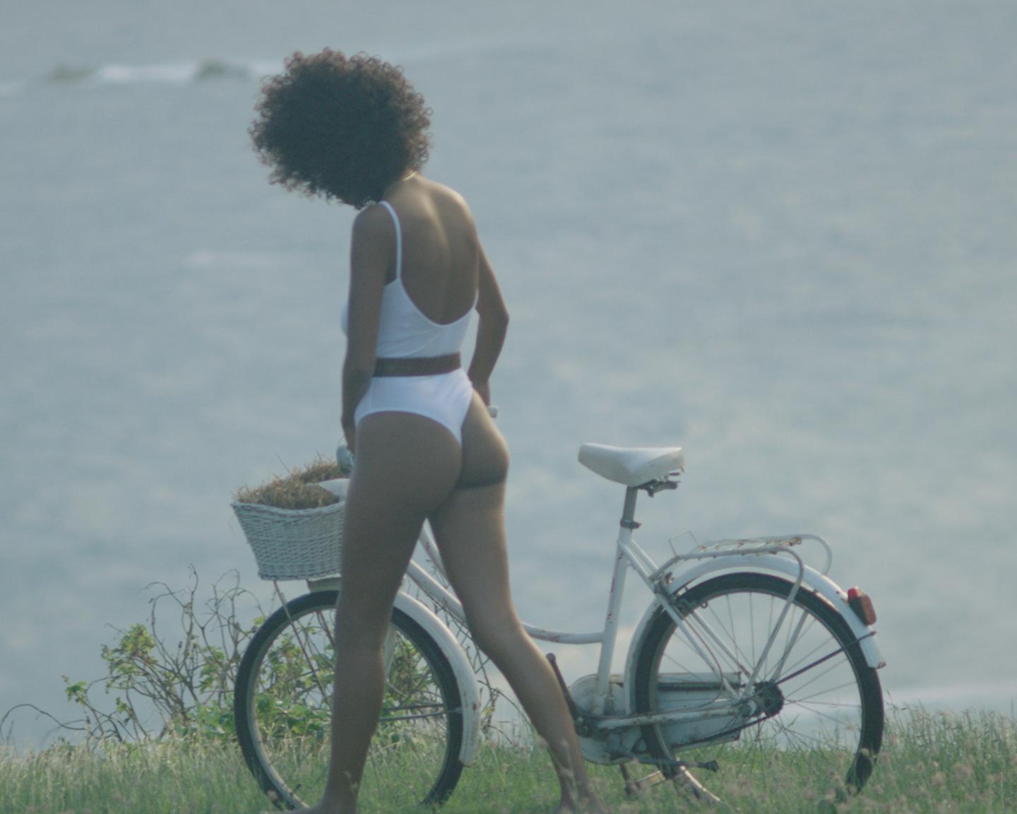 Playboy Playmate (Nereyda Bird): Nereyda und ihr kleines weißes Fahrrad erklimmen die Steilküsten hoch über dem Meer und bieten uns die ganze Zeit über einen atemberaubenden Blick